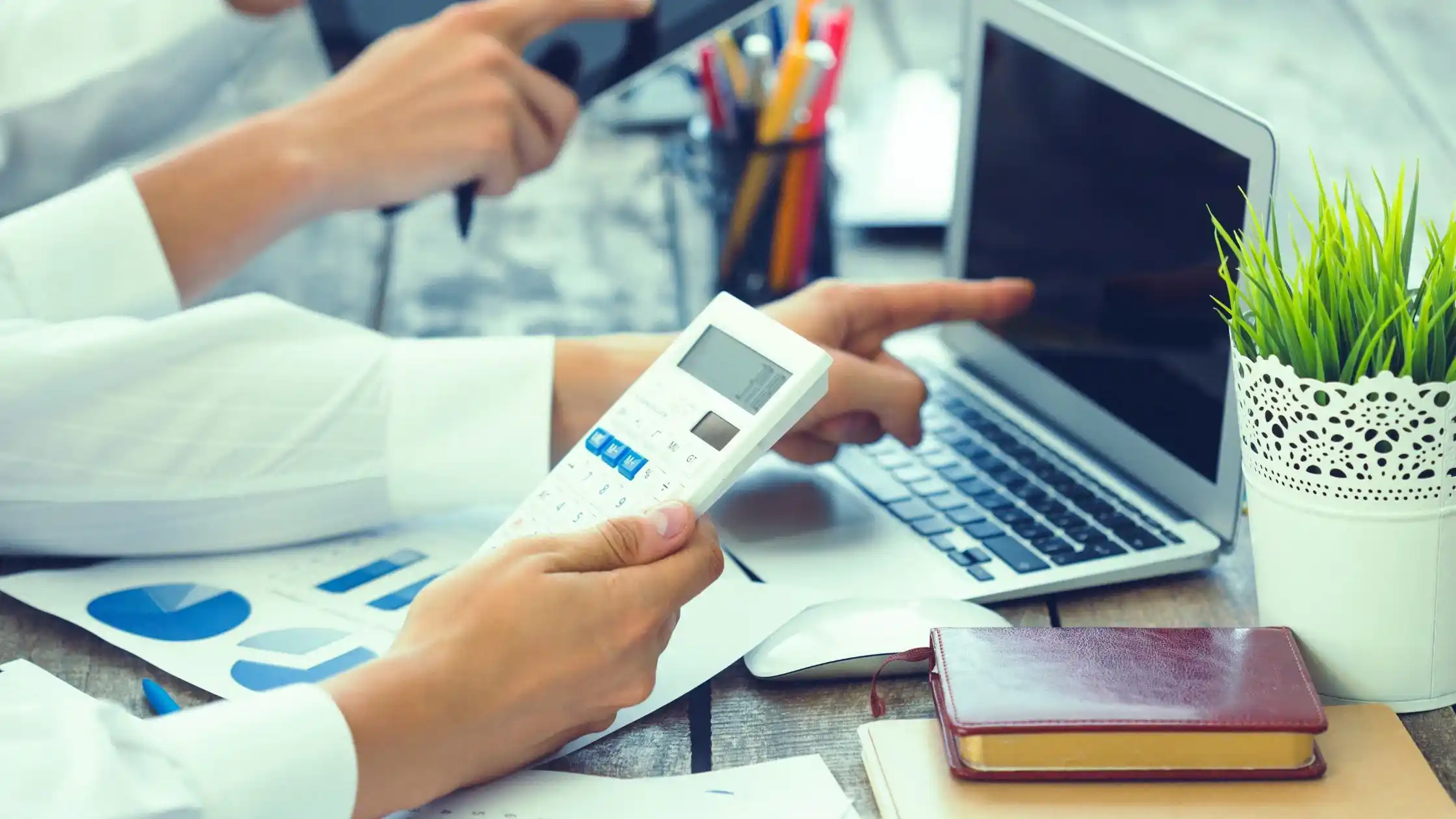 Payroll audit and financial review process in a UAE office, showing professionals analyzing payroll data on a laptop with a calculator and financial reports.
